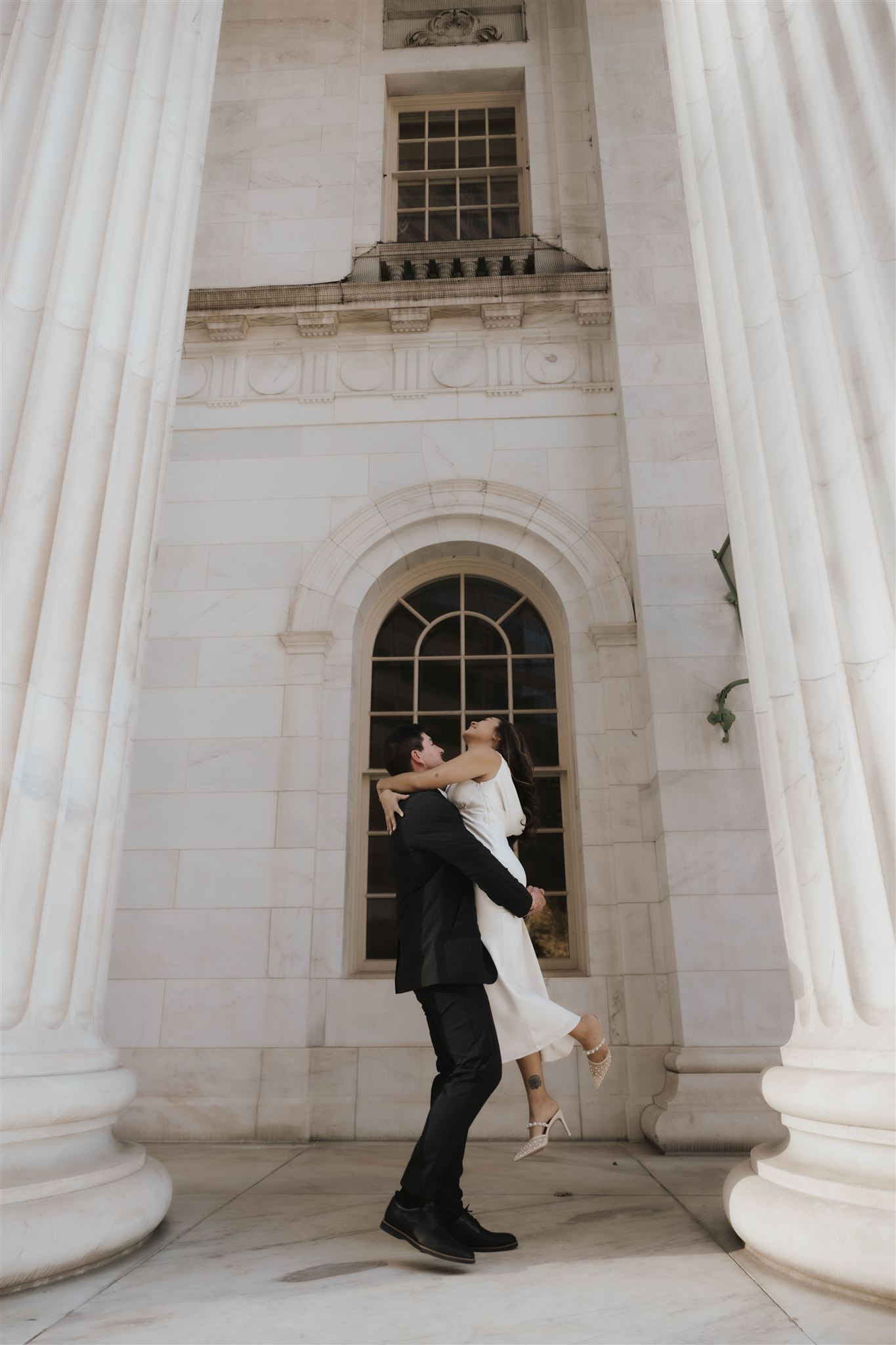 a man picking up his soon to be wife between the courthouse pillars during their Elegant Engagement Photos