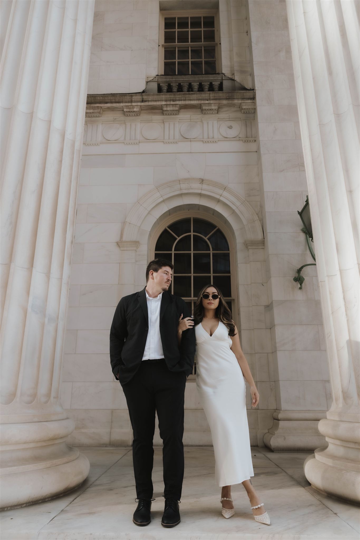 a man and woman posing between white pillars for their Elegant Engagement Photos