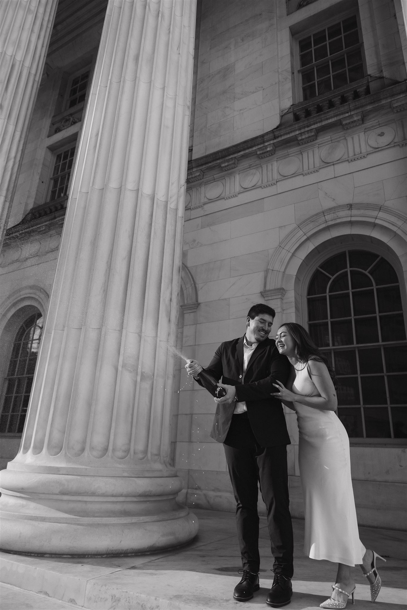 black and white of a newly engaged couple popping champagne 