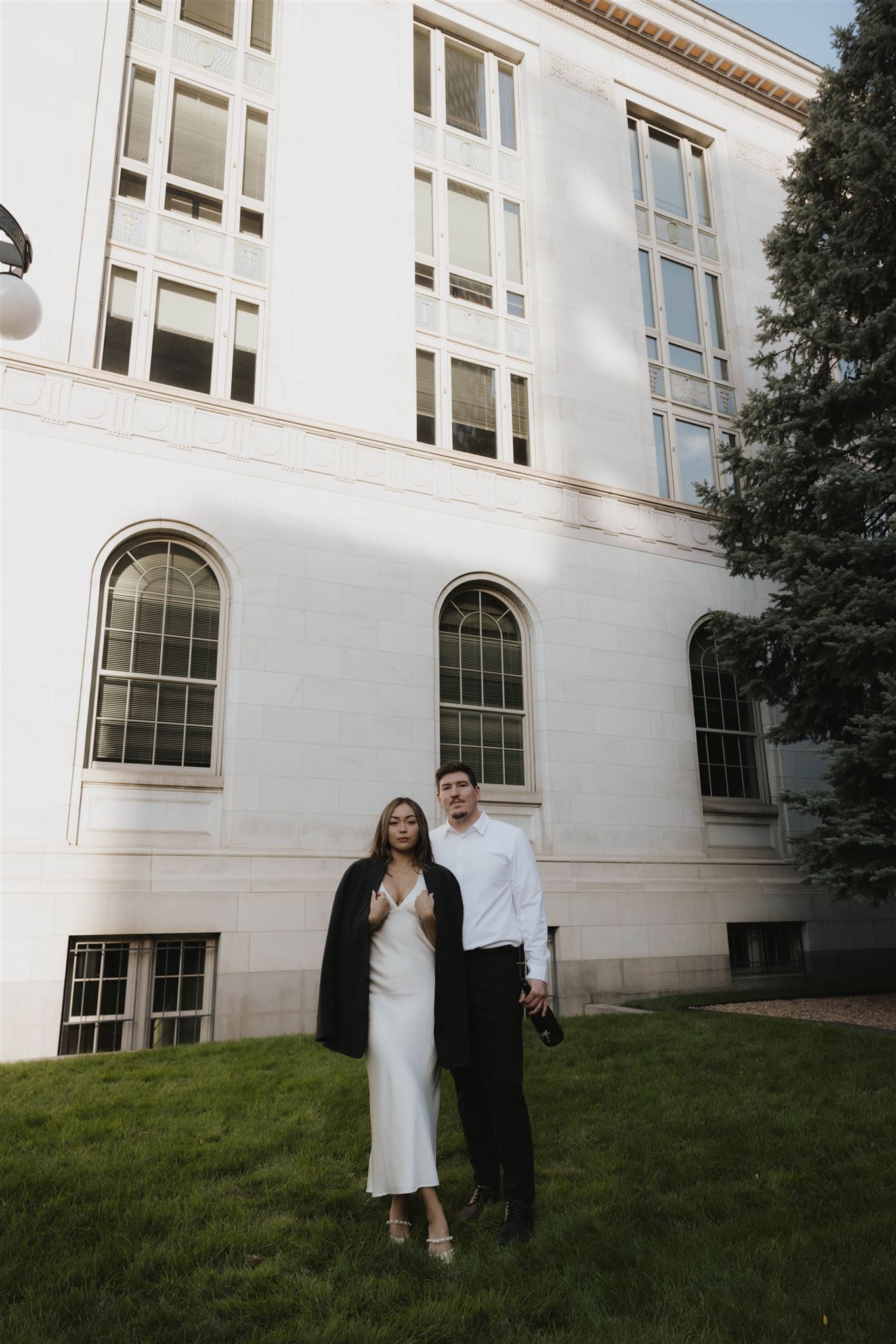 a woman wearing a man's jacket while he stands beside her during their Elegant Engagement Photos