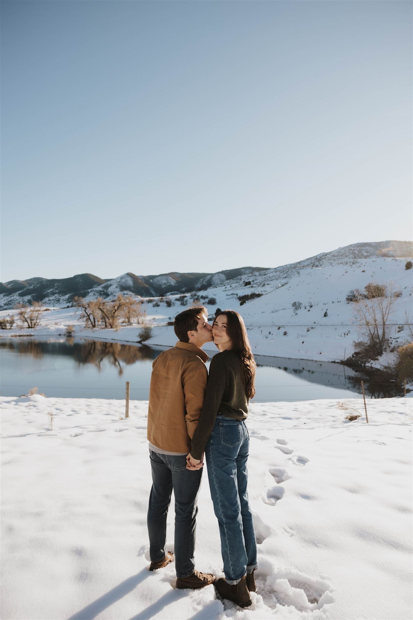 a man kissing a woman on the cheek during their Snowy Engagement Photos