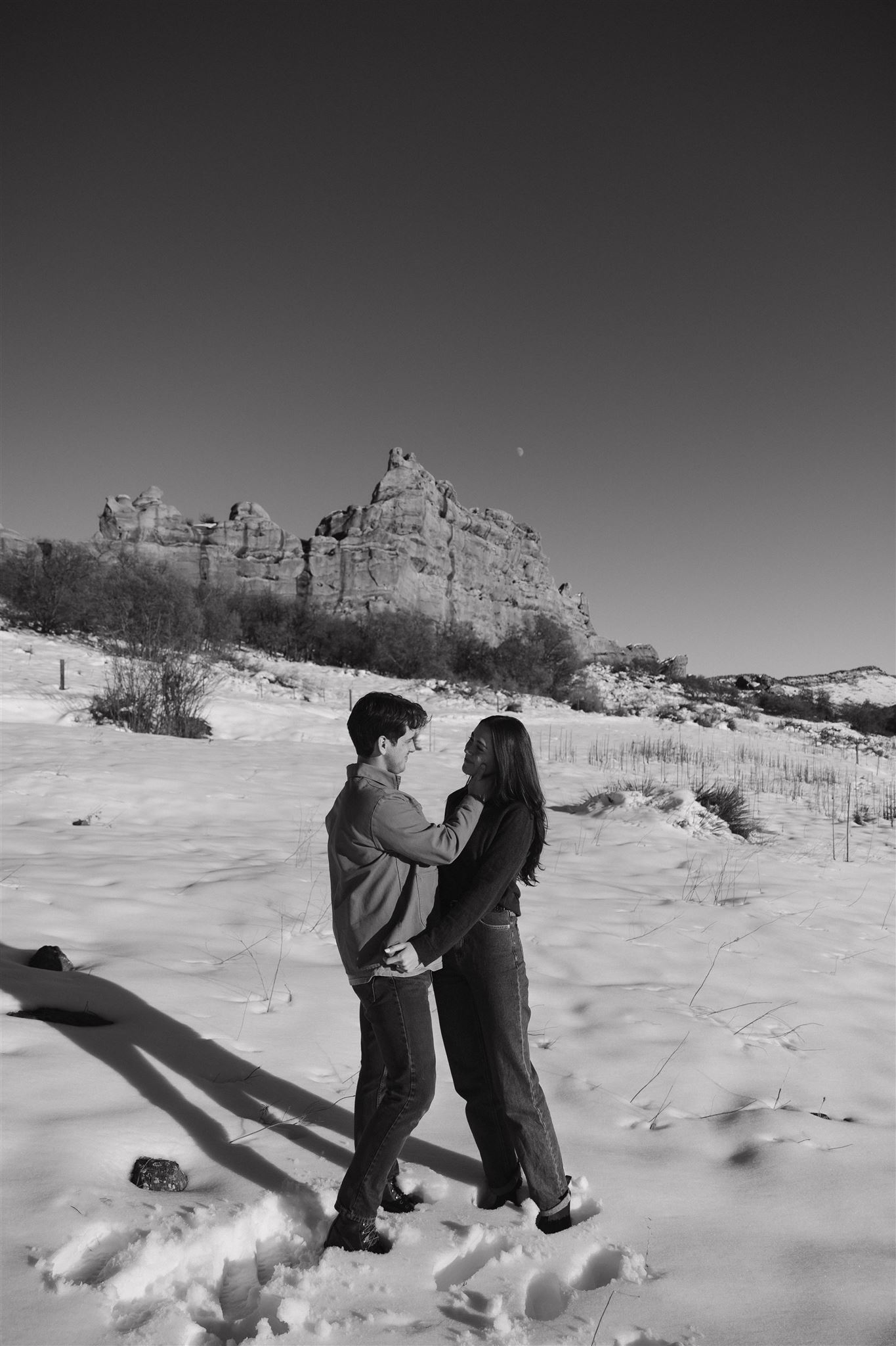 a man touching a woman's face as she smiles at him during their Snowy Engagement Photos