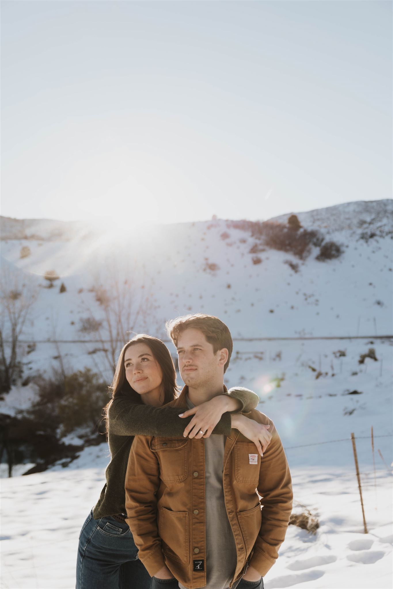 newly engaged couple looking off into the distance together in the snow 