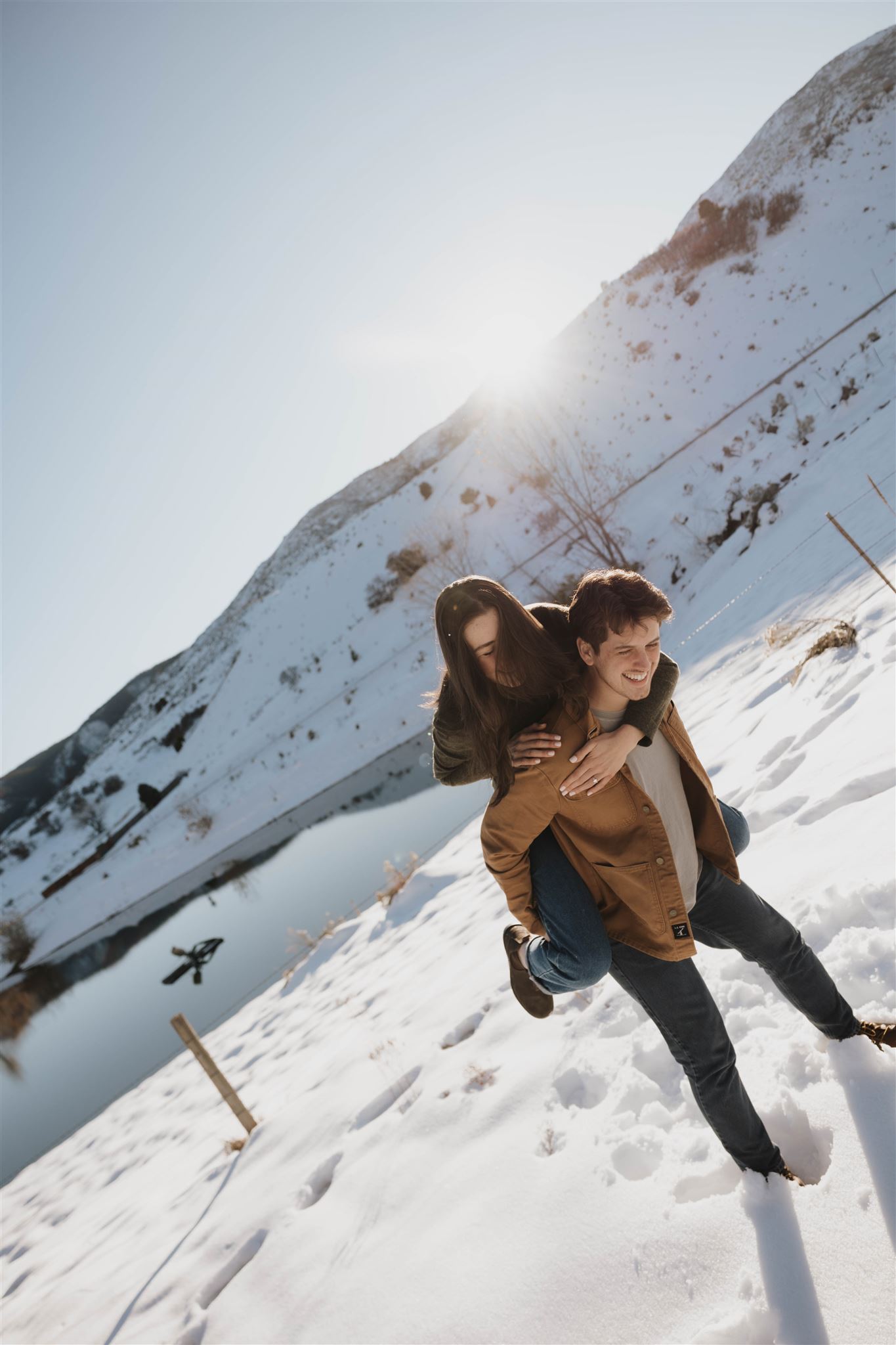 a woman riding on a man's back during their Snowy Engagement Photos