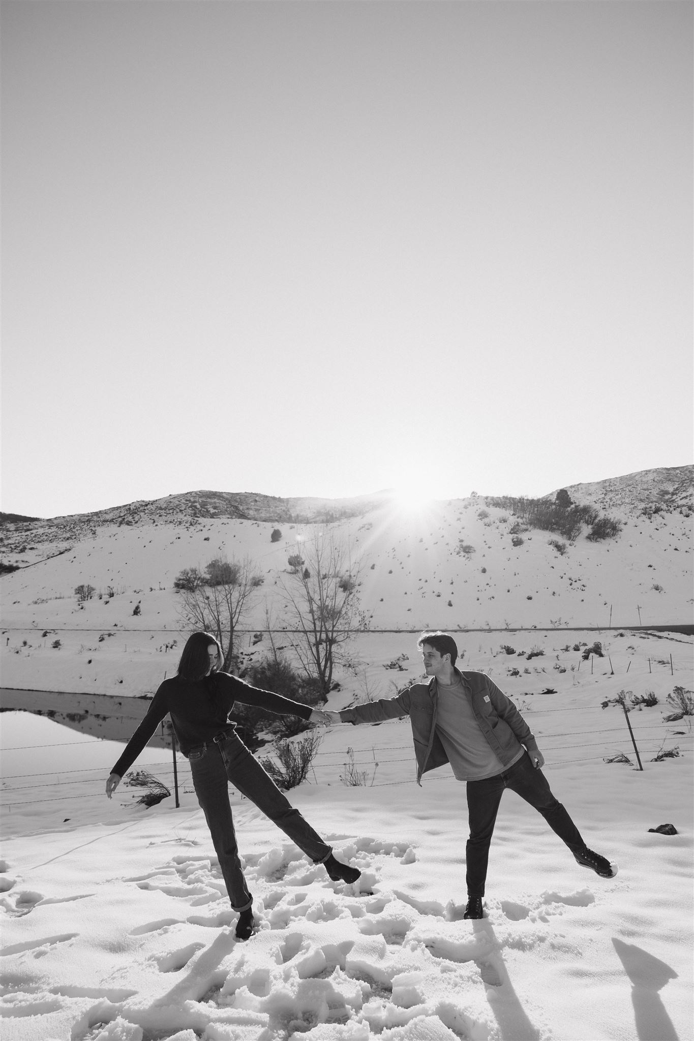 a couple holding hands and leaning to the side together during their Snowy Engagement Photos