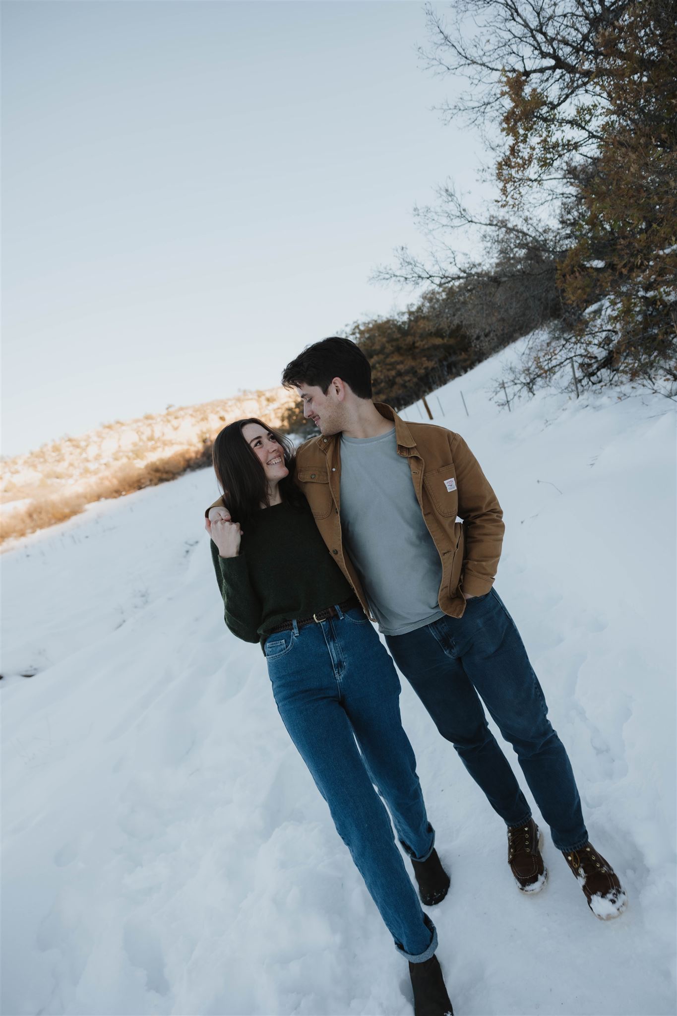 newly engaged couple walking while holding each other in the snow 