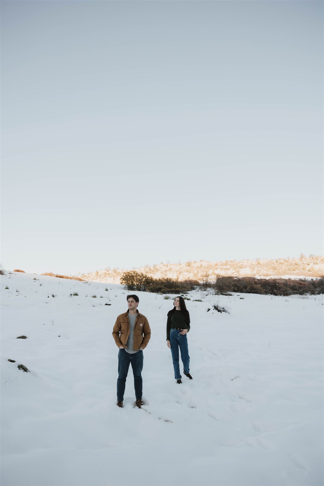 a man and woman standing in the snow looking off into the distance 