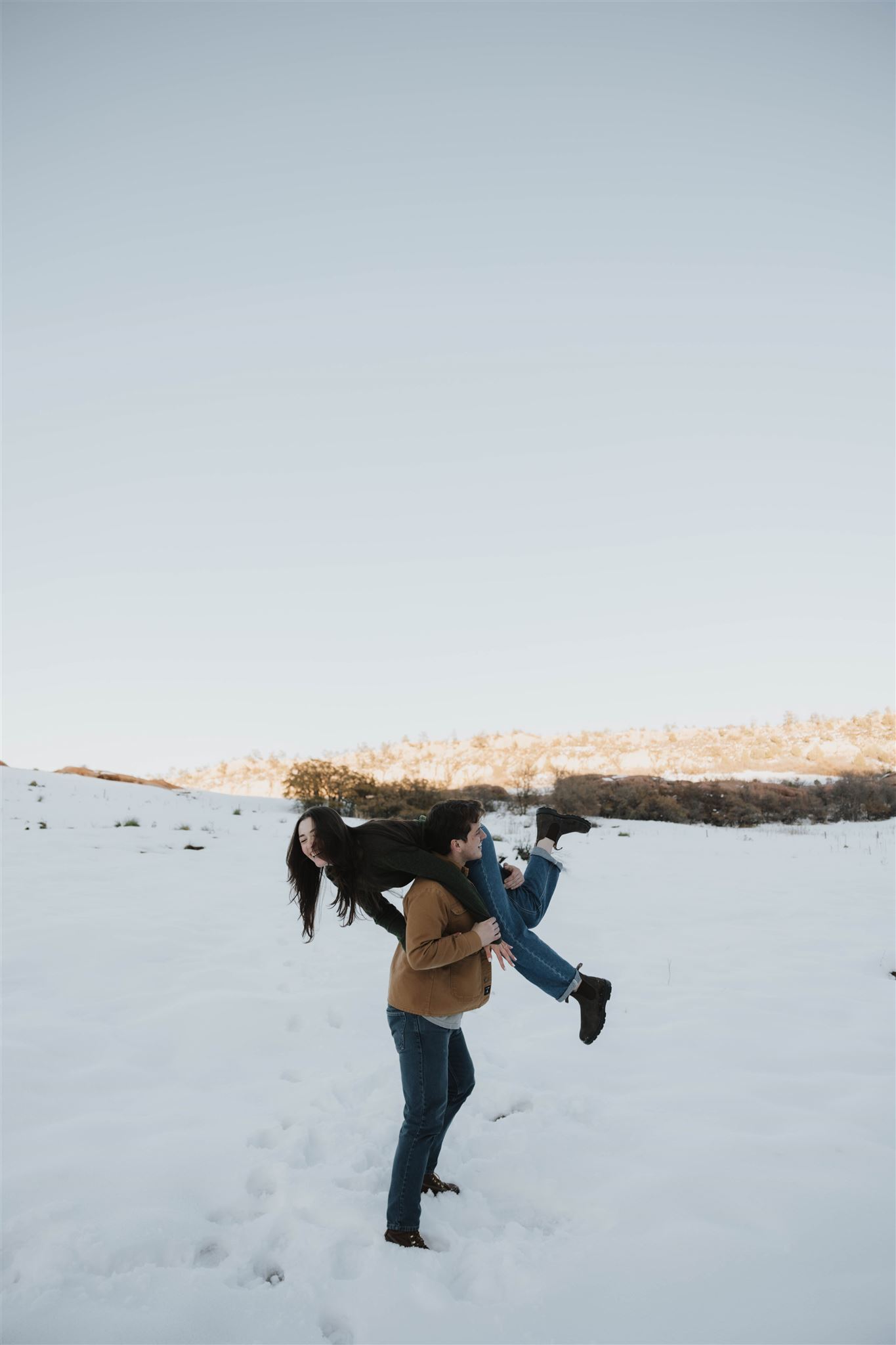 a man holding a woman over his shoulder during their Snowy Engagement Photos