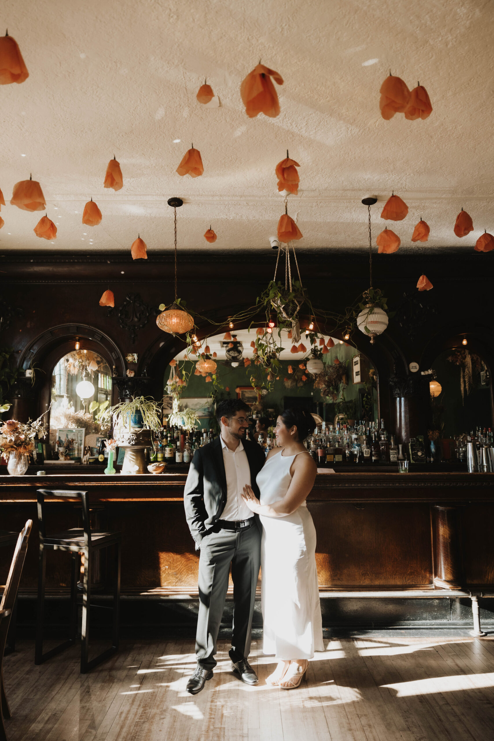 newly engaged couple standing in a bar with flowers hanging from the ceiling 