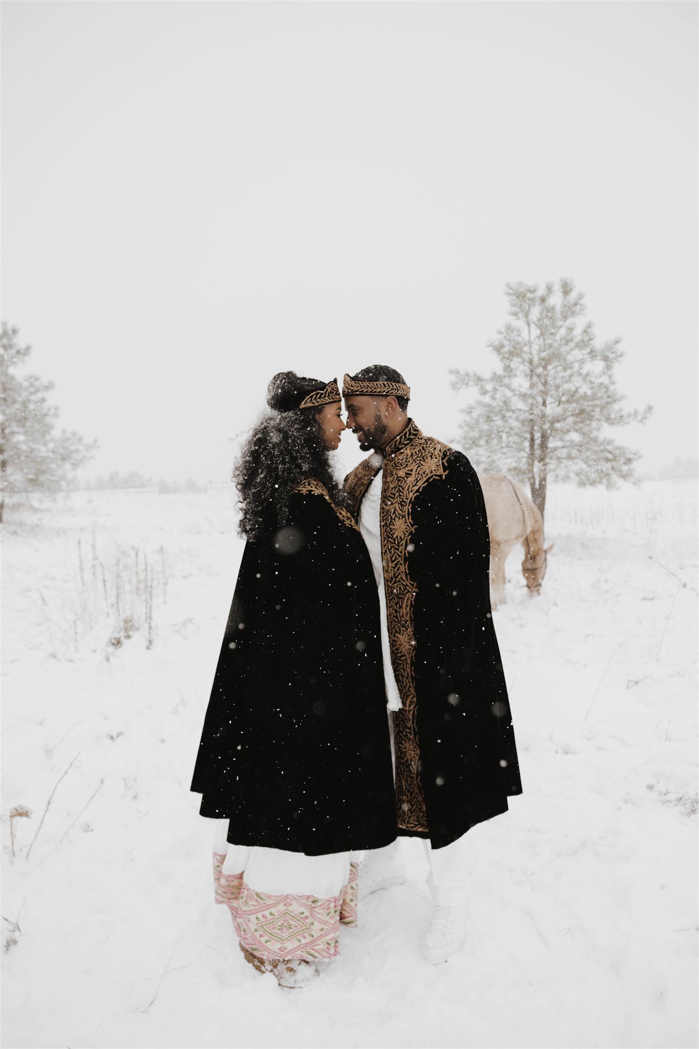 newly engaged couple with their heads together as it snows on them 